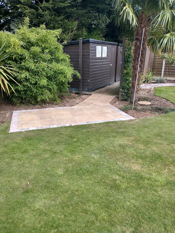 A composite garden shed set square on a neatly laid porcelain-and-brick base, tucked beside established bamboo and a palm — a proper level base built to take the structure.