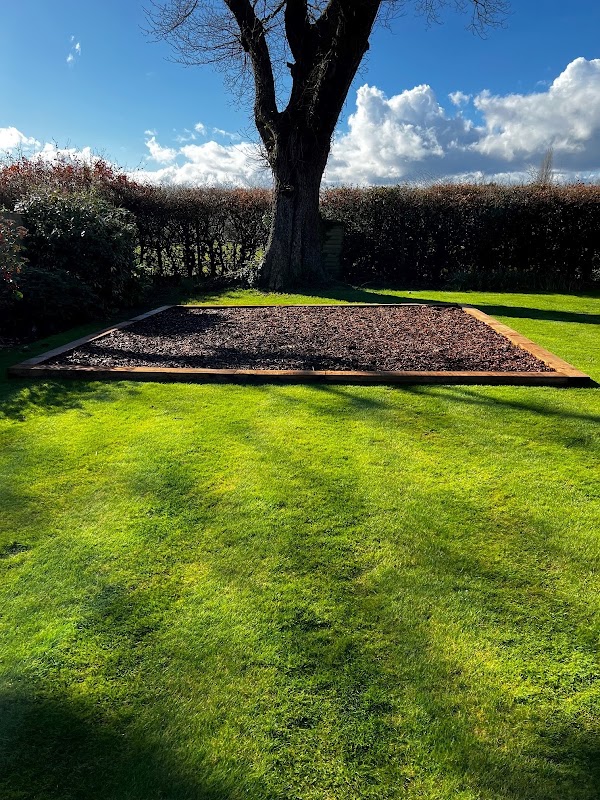 A concrete slab base cast and edged with timber on a lawn beneath a mature tree — the prepared foundation for an outbuilding or hot tub.